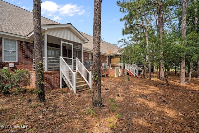 back of property with a sunroom, brick siding, a shingled roof, and stairs