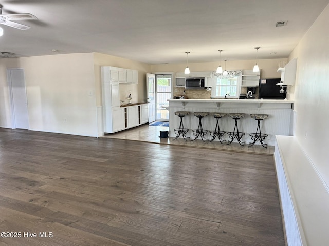 3306 E Oak Island Dr, Oak Island, NC 28465 - kitchen featuring stainless steel microwave, black fridge, white cabinets, dark wood-style flooring, and a breakfast bar area