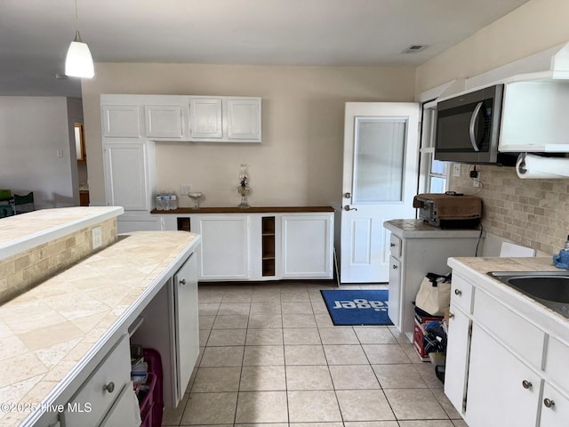 3306 E Oak Island Dr, Oak Island, NC 28465 - kitchen with tile countertops, white cabinets, backsplash, hanging light fixtures, and light tile patterned floors