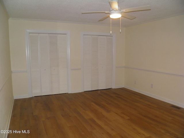 unfurnished bedroom with multiple closets, wood finished floors, crown molding, baseboards, and a textured ceiling
