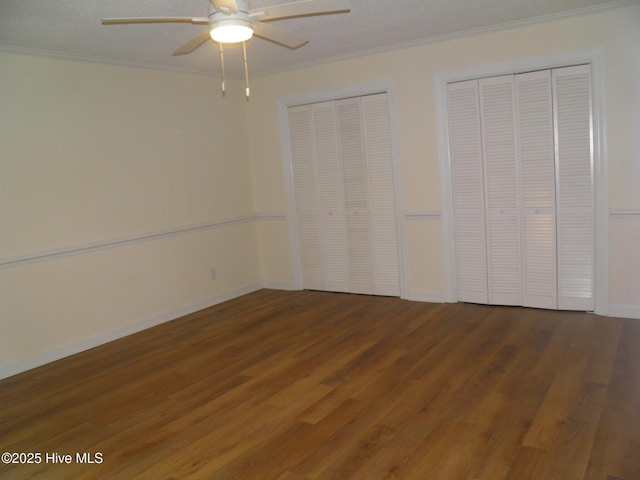 unfurnished bedroom with two closets, crown molding, wood finished floors, baseboards, and ceiling fan