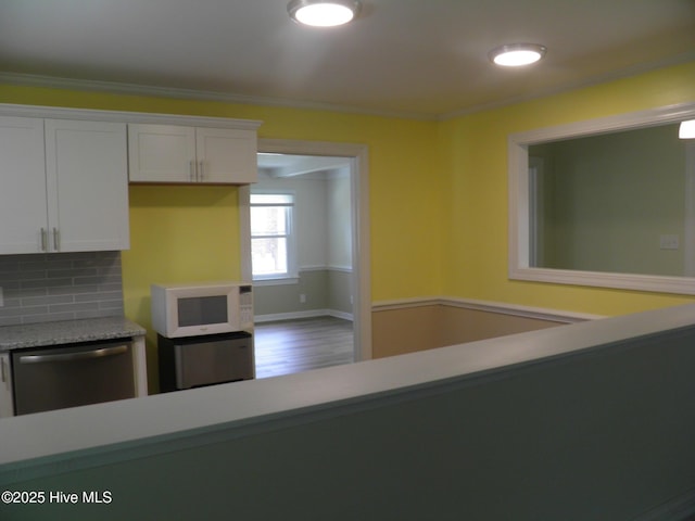 kitchen featuring white microwave, stainless steel dishwasher, light countertops, white cabinets, and ornamental molding