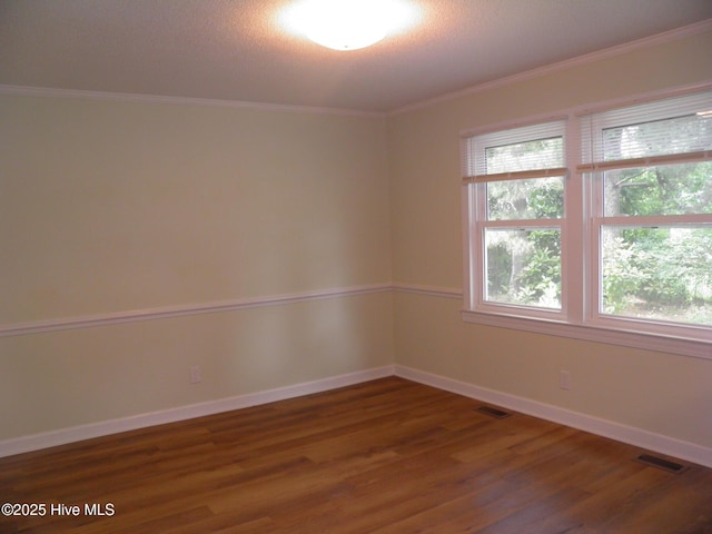 empty room featuring wood finished floors, plenty of natural light, crown molding, and baseboards