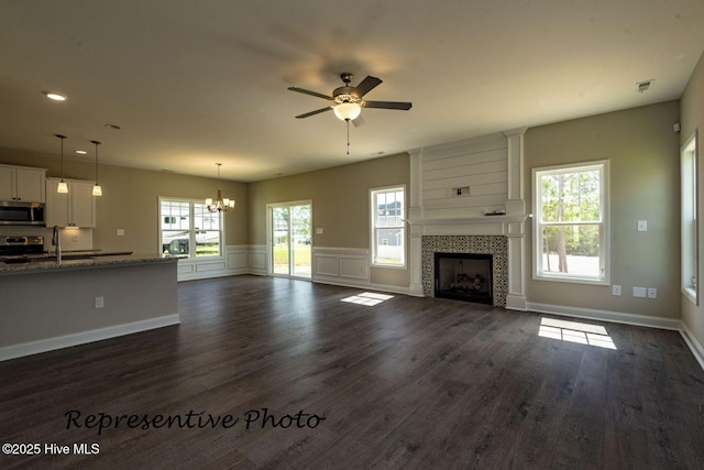 30080 Loblolly Ct, Wagram, NC 28396 - unfurnished living room with a ceiling fan, a chandelier, a tile fireplace, dark wood-style floors, and wainscoting