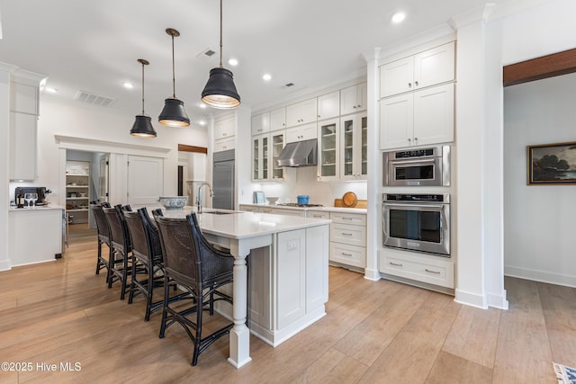 kitchen featuring stainless steel built in refrigerator, under cabinet range hood, light countertops, white cabinets, and a large island with sink