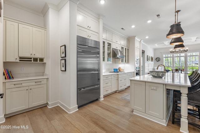 kitchen with built in refrigerator, under cabinet range hood, white gas stovetop, a breakfast bar area, and light wood finished floors