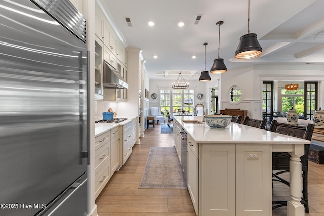 kitchen with stainless steel appliances, a breakfast bar area, under cabinet range hood, a sink, and light countertops