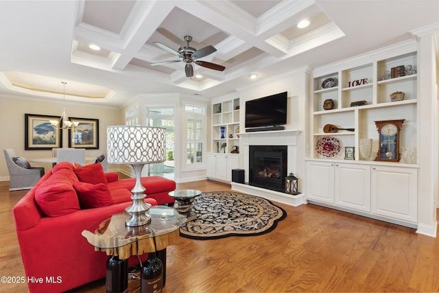 living area with ornamental molding, a glass covered fireplace, light wood-style flooring, ceiling fan, and coffered ceiling