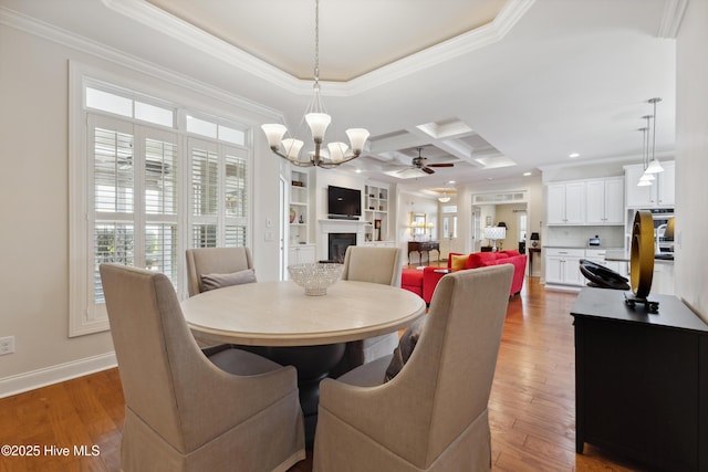 dining room with a ceiling fan, crown molding, a fireplace, coffered ceiling, and a chandelier