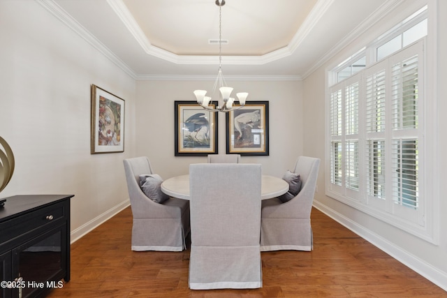 dining area with a chandelier, a raised ceiling, wood finished floors, baseboards, and crown molding
