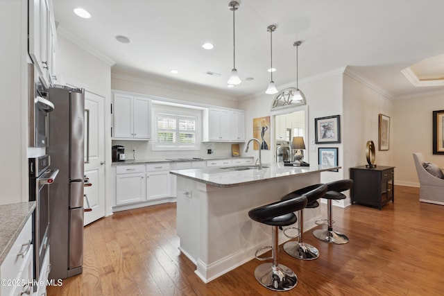 kitchen featuring a sink, light wood-style flooring, a breakfast bar area, white cabinets, and ornamental molding