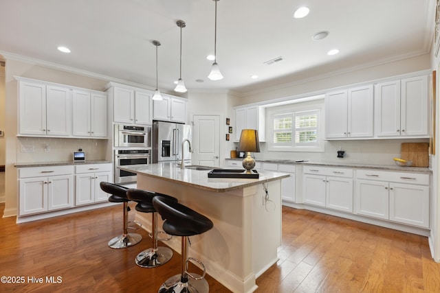 kitchen featuring stainless steel appliances, ornamental molding, a kitchen breakfast bar, white cabinetry, and a sink