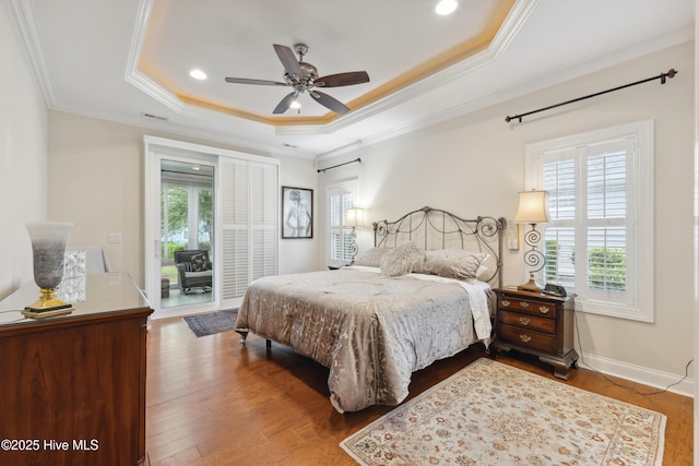 bedroom with multiple windows, a raised ceiling, access to outside, ornamental molding, and dark wood-style floors