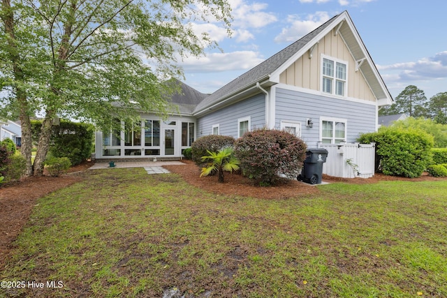 rear view of house featuring board and batten siding, a sunroom, roof with shingles, and a lawn