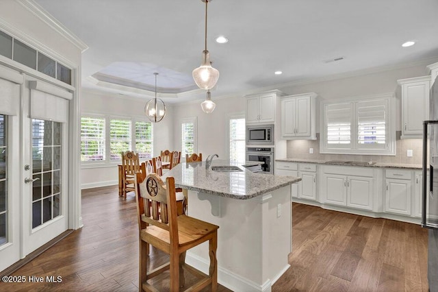 kitchen with appliances with stainless steel finishes, a sink, dark wood-type flooring, ornamental molding, and white cabinets