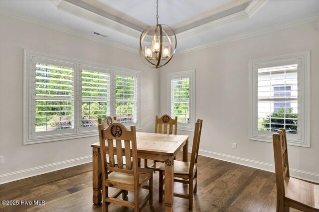 dining space featuring dark wood-type flooring, a chandelier, ornamental molding, baseboards, and a raised ceiling