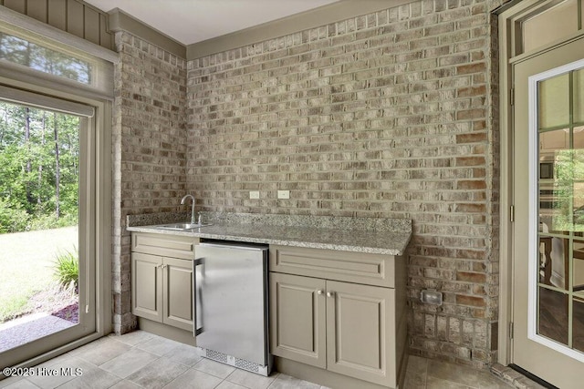 indoor wet bar featuring fridge, brick wall, and light tile patterned floors