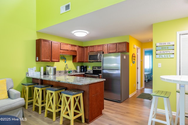 kitchen featuring appliances with stainless steel finishes, a peninsula, light wood-type flooring, a breakfast bar area, and light stone countertops
