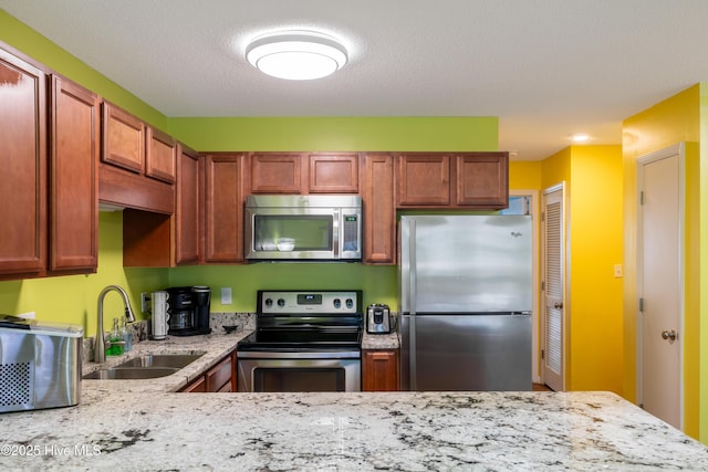 kitchen with appliances with stainless steel finishes, a sink, and light stone counters