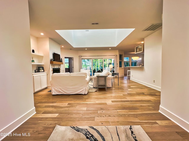 living area featuring light wood finished floors, a fireplace, a skylight, baseboards, and recessed lighting