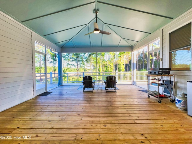 unfurnished sunroom with a ceiling fan, lofted ceiling, wooden walls, wood-type flooring, and a deck