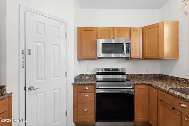 kitchen with appliances with stainless steel finishes, dark stone countertops, and brown cabinets