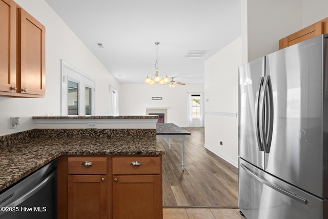 kitchen with stainless steel appliances, a chandelier, a peninsula, and brown cabinets