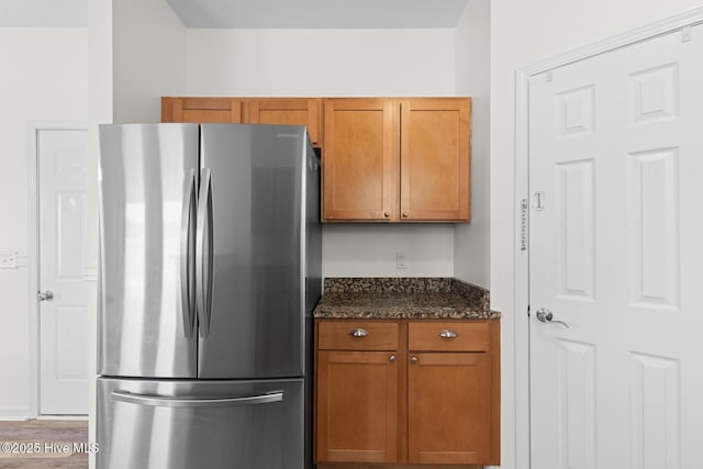 kitchen with freestanding refrigerator, dark stone counters, brown cabinets, and wood finished floors