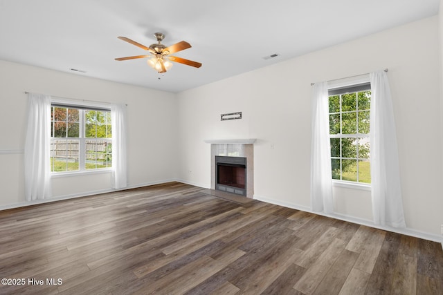unfurnished living room featuring healthy amount of natural light, wood finished floors, a tiled fireplace, and a ceiling fan