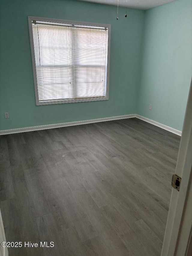 spare room featuring baseboards and dark wood-style floors
