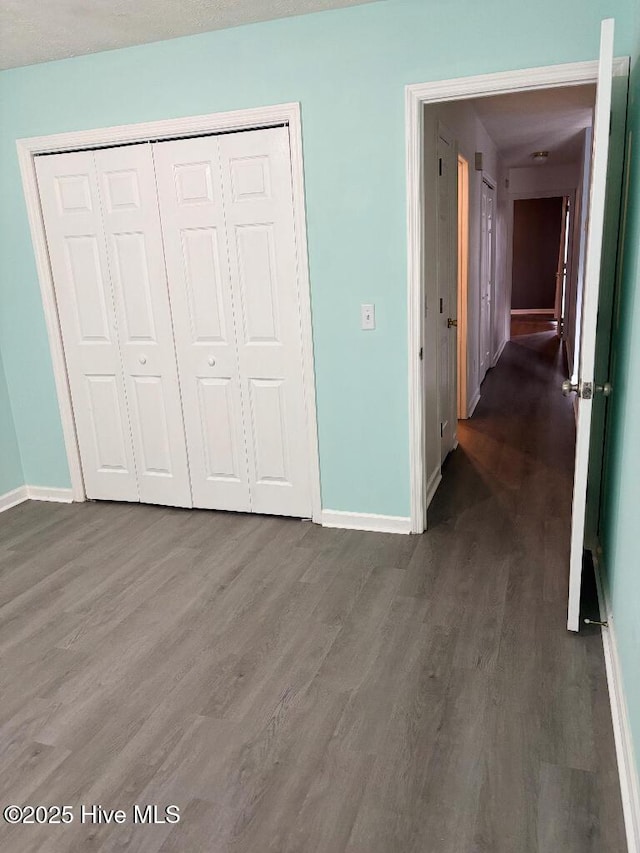 unfurnished bedroom featuring baseboards, wood finished floors, and a closet