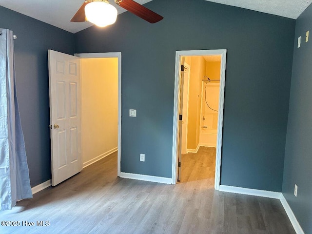unfurnished bedroom with wood finished floors, vaulted ceiling, baseboards, and a ceiling fan