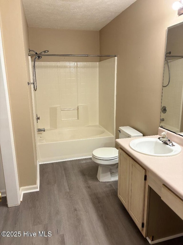 bathroom with wood finished floors, a textured ceiling, toilet, vanity, and  shower combination