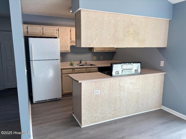 kitchen with freestanding refrigerator, a sink, light countertops, wood finished floors, and baseboards