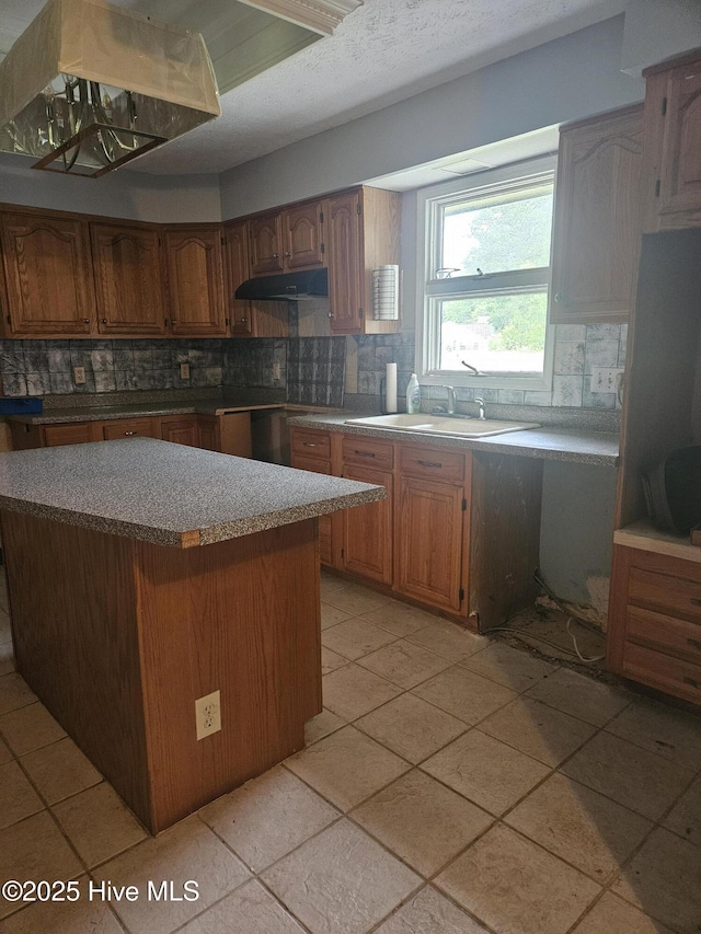4 Cleek Ct, Carolina Shores, NC 28467 - kitchen with backsplash, under cabinet range hood, a sink, a center island, and brown cabinets