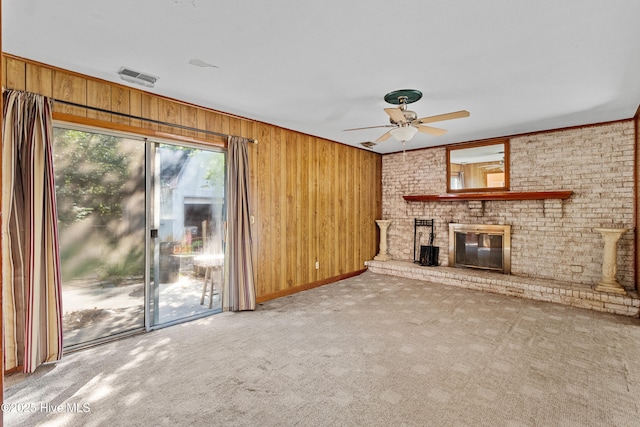 unfurnished living room with a ceiling fan, a brick fireplace, wood walls, and carpet floors