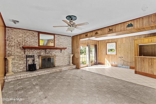 unfurnished living room featuring wooden walls, ceiling fan, a fireplace, and carpet
