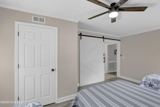 bedroom featuring wood finished floors, crown molding, a barn door, baseboards, and ceiling fan
