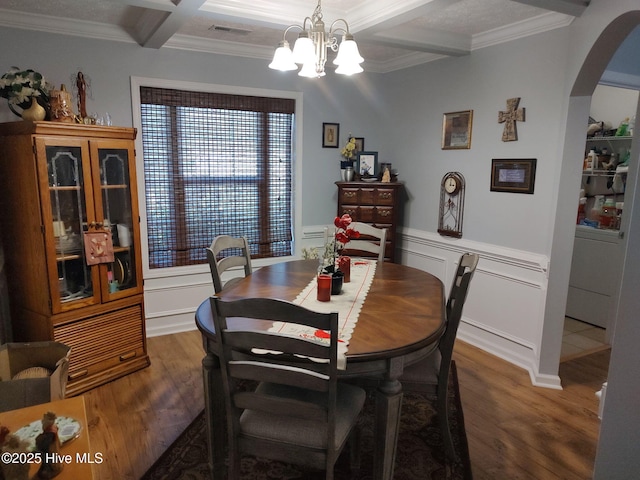 dining space featuring arched walkways, wood finished floors, crown molding, a chandelier, and beam ceiling