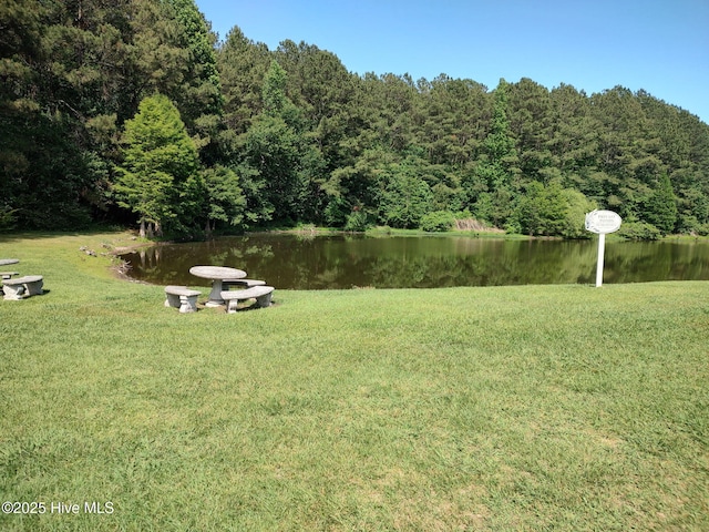 view of green lawn featuring a water view and a wooded view
