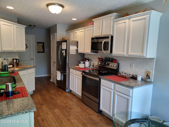 kitchen featuring stainless steel appliances, white cabinets, a textured ceiling, tasteful backsplash, and wood finished floors