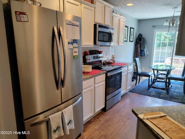 kitchen featuring stainless steel appliances, tasteful backsplash, light wood-style floors, a textured ceiling, and white cabinetry