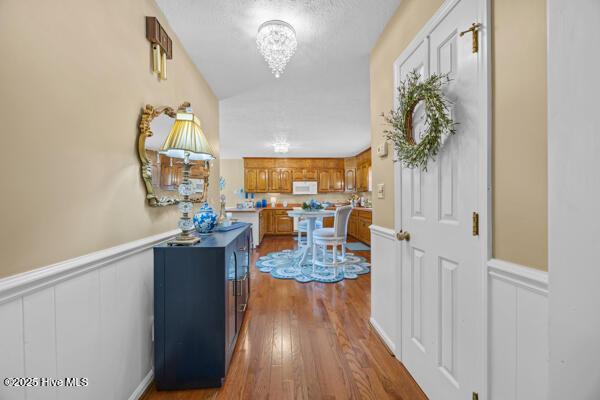 hall featuring a chandelier, dark wood-type flooring, wainscoting, vaulted ceiling, and a decorative wall