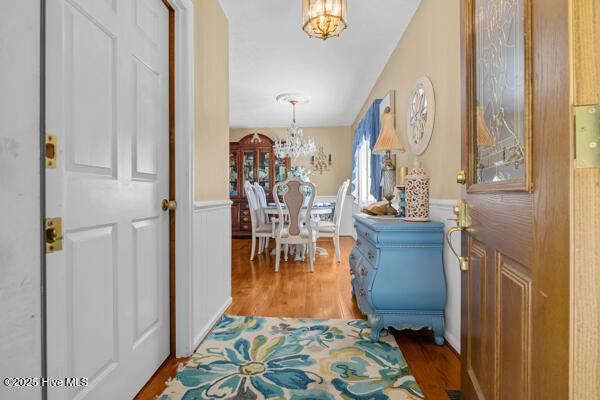 entrance foyer featuring a chandelier, light wood finished floors, a wainscoted wall, and a decorative wall