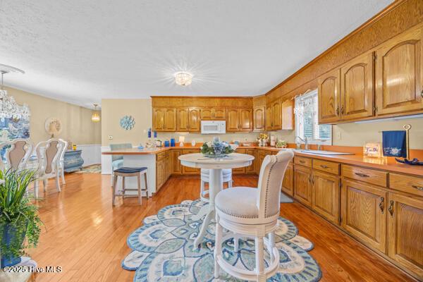 kitchen featuring white microwave, a peninsula, light countertops, and brown cabinets