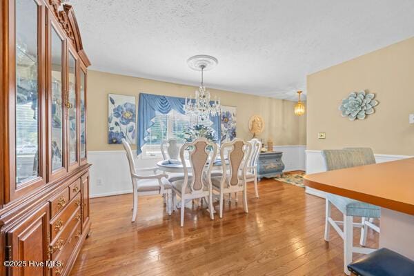dining space featuring wainscoting, light wood-type flooring, a chandelier, and a textured ceiling