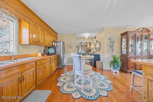 kitchen featuring light countertops, a sink, brown cabinets, light wood finished floors, and a wainscoted wall