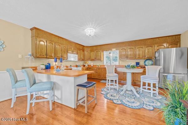 kitchen with freestanding refrigerator, white microwave, a peninsula, light countertops, and a breakfast bar