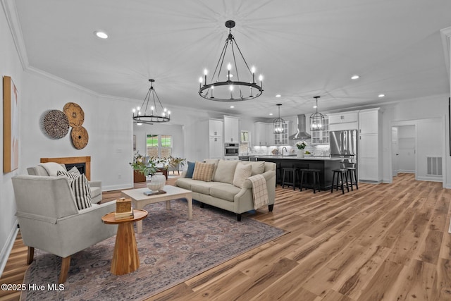 living room featuring a chandelier, light wood-type flooring, recessed lighting, ornamental molding, and baseboards