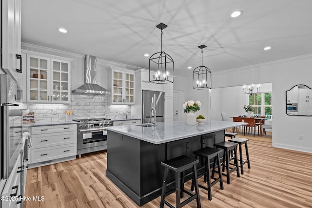 kitchen with wall chimney exhaust hood, appliances with stainless steel finishes, a chandelier, white cabinets, and recessed lighting